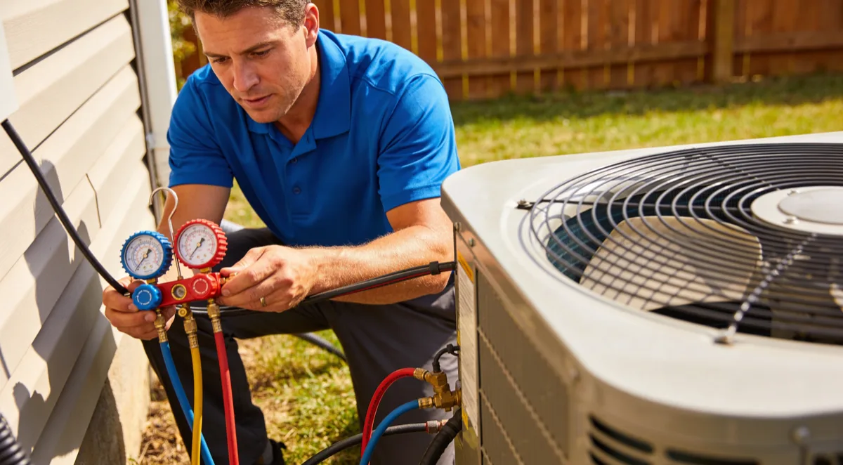 Técnico de reparación de aire acondicionado verificando presión de refrigerante con manómetros en unidad exterior