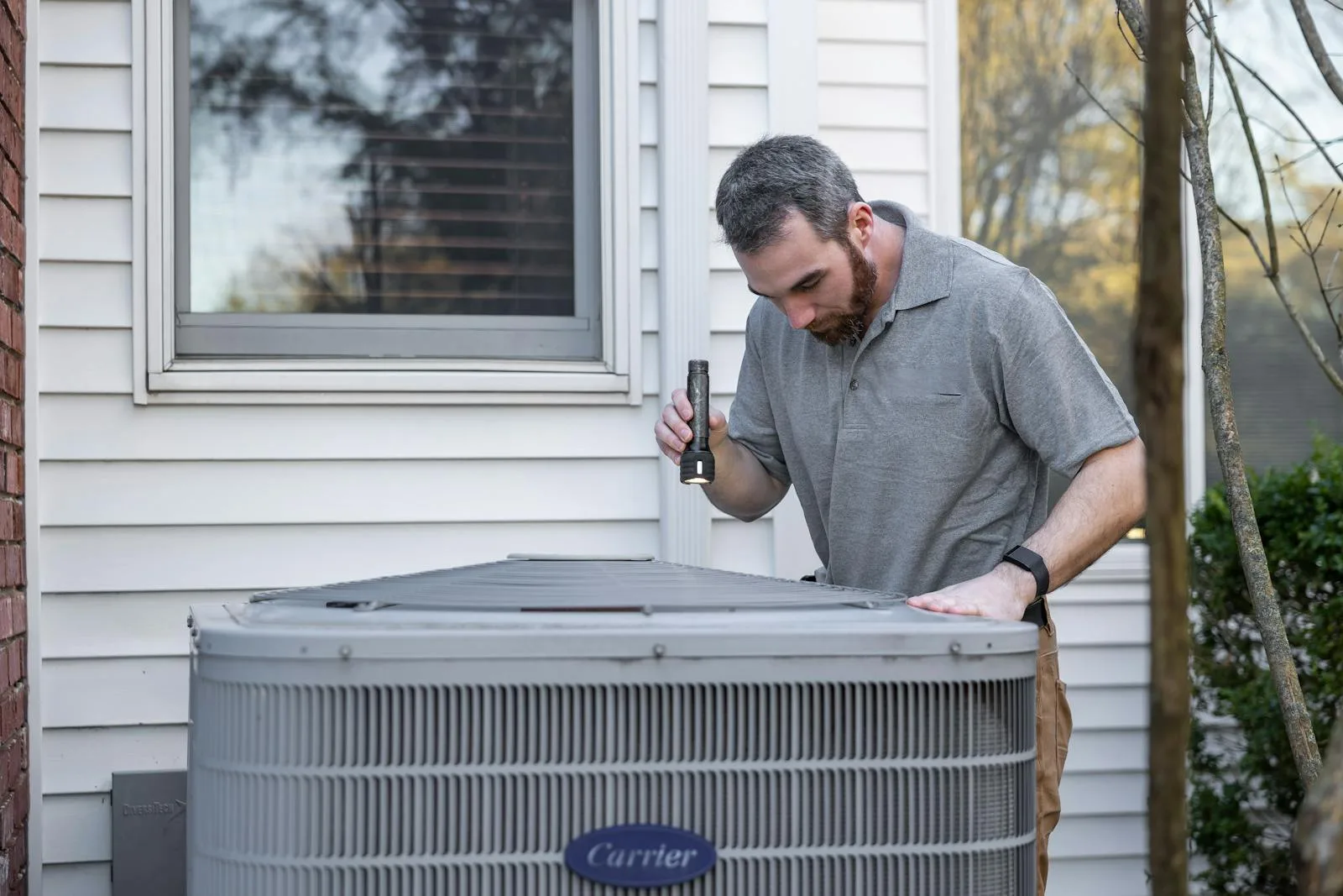 HVAC technician inspecting an outdoor AC condenser during a seasonal maintenance visit in East Alabama